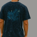 Person wearing a dark blue t-shirt with a palm leaf design on the back against a gray background