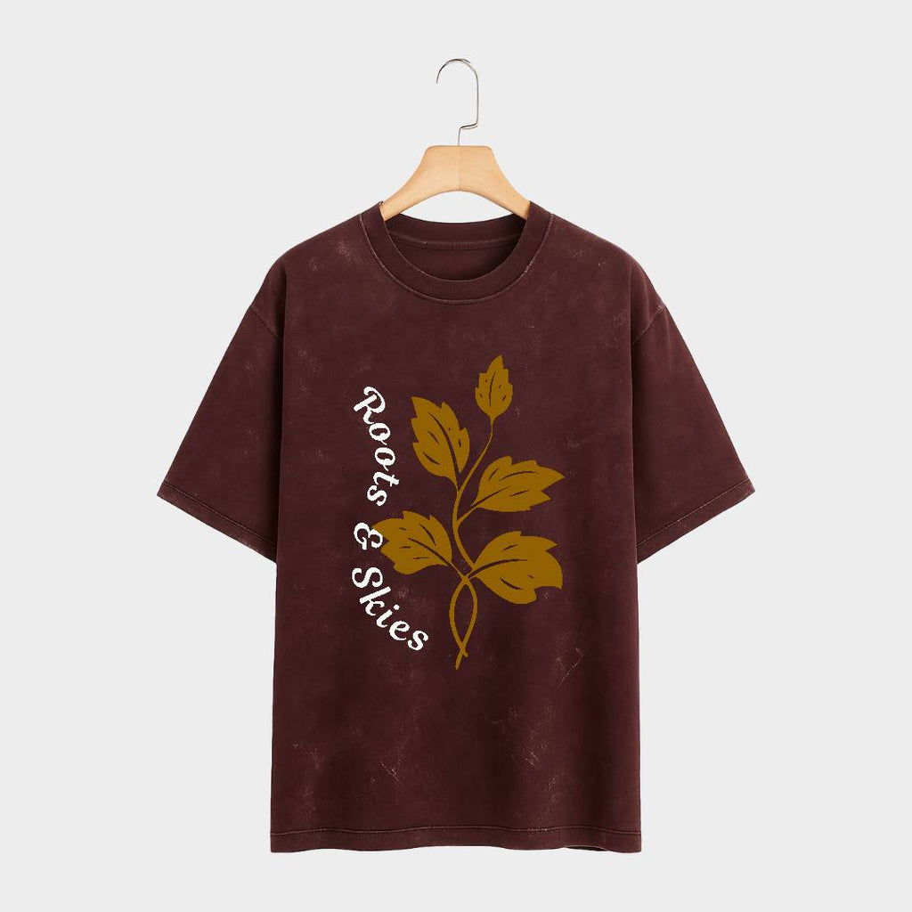 Brown t-shirt with leaf design and 'Roots & Skies' text on a hanger against a white background