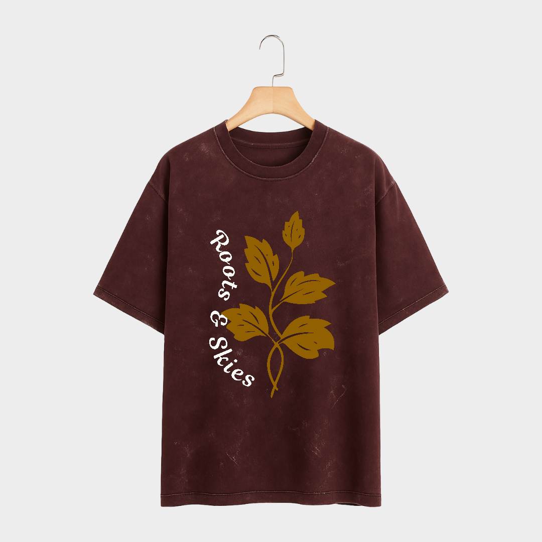 Brown t-shirt with leaf design and 'Roots & Skies' text on a hanger against a white background